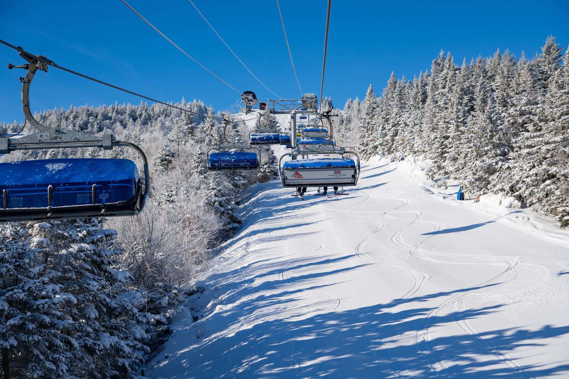 Snow-covered ski lift chairs gliding over a pristine powder slope with frosted trees.