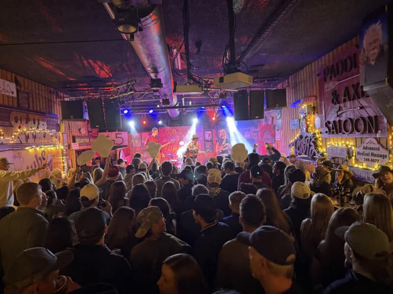 Crowd enjoying live music at a mountain town bar with colorful lights and graffiti decor.