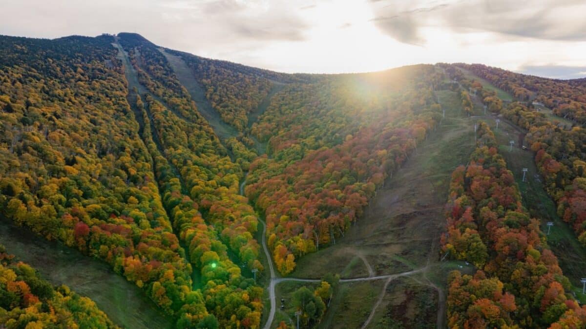 Colorful fall foliage on mountain slopes with ski trails and lifts.