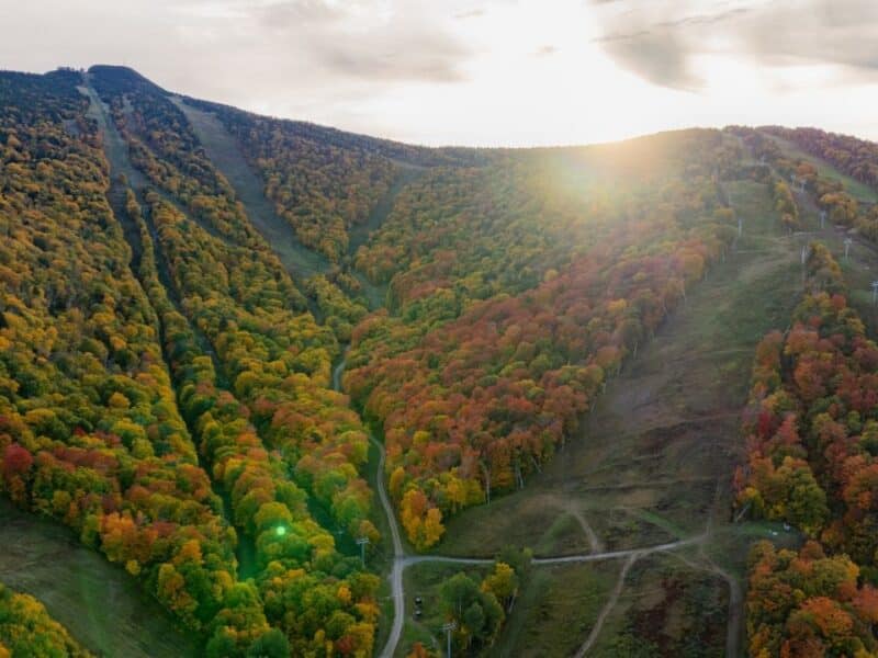 Colorful fall foliage on mountain slopes with ski trails and lifts.
