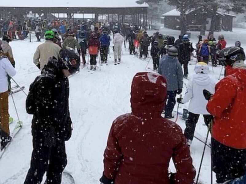 Large group of skiers and snowboarders gathering at snowy mountain resort.