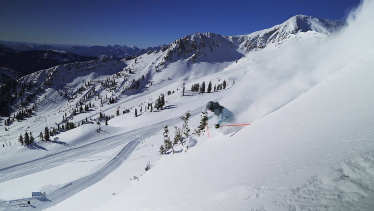 Snowboarder carving through fresh mountain snow with scenic peaks.