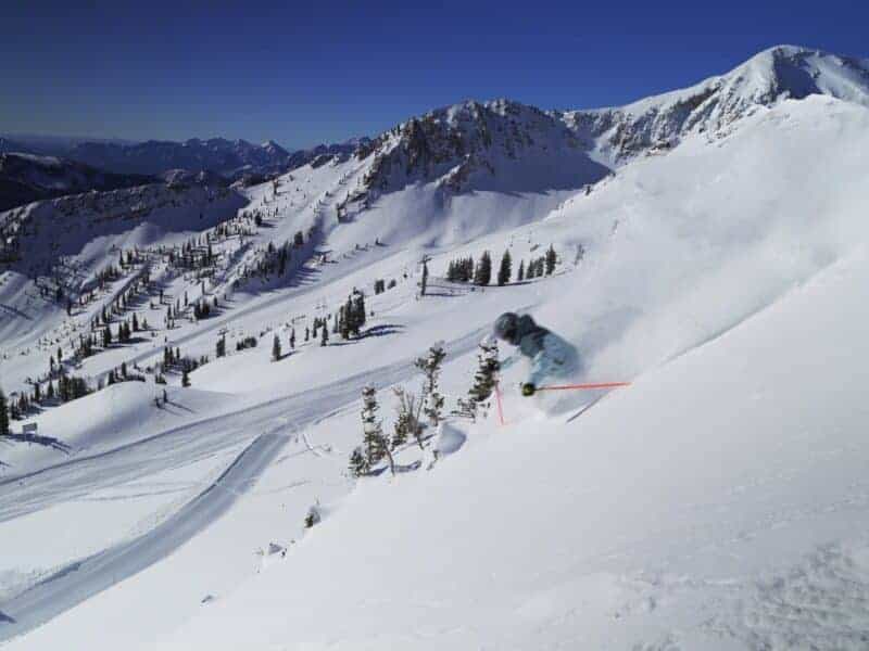 Snowboarder carving through fresh mountain snow with scenic peaks.