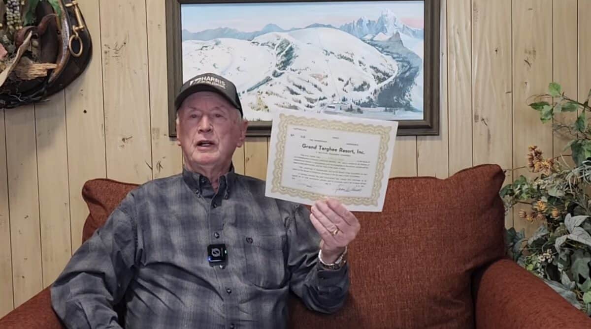 Elderly man holding a certificate in a cozy mountain lodge setting.