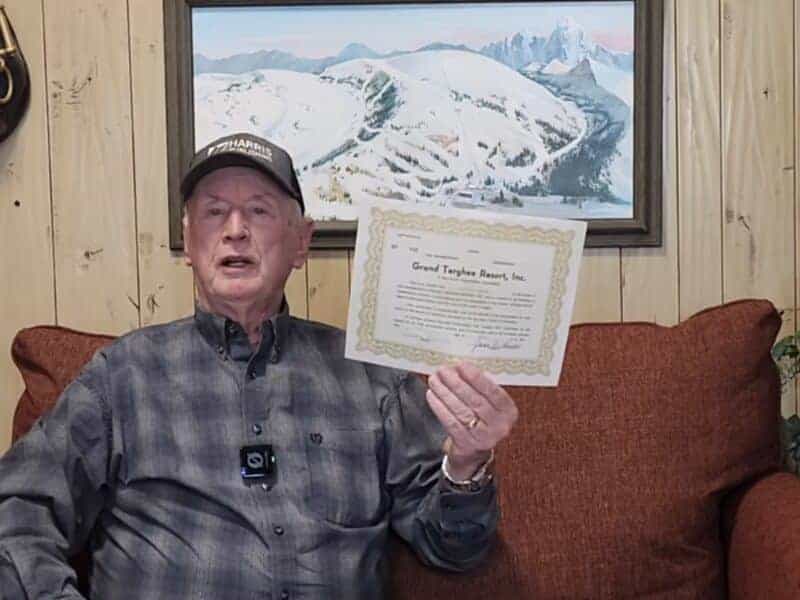 Elderly man holding a certificate in a cozy mountain lodge setting.