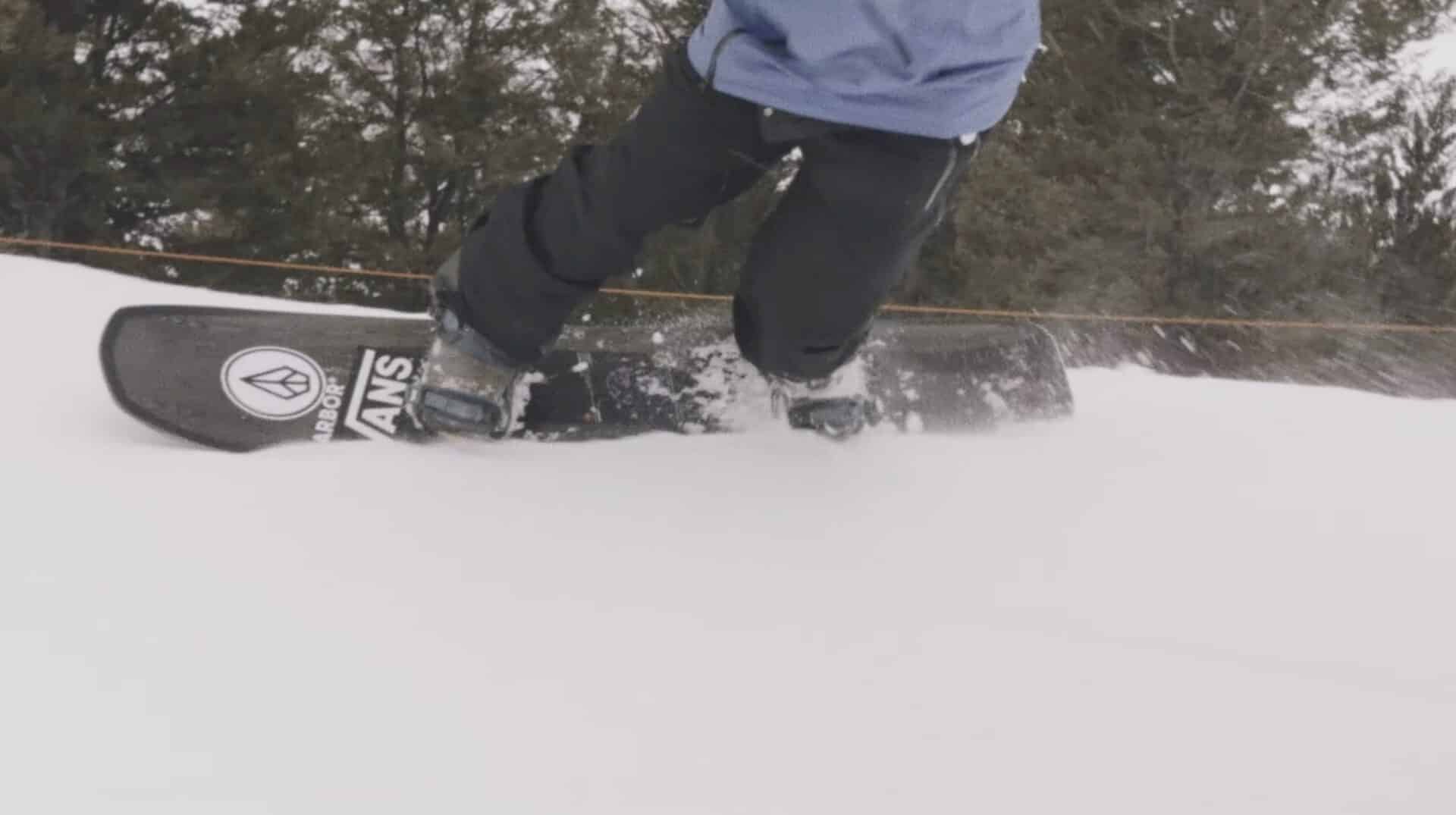 Close-up of snowboarder riding on snow with trees in background.