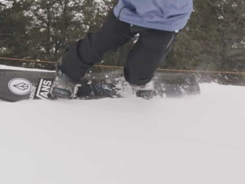 Close-up of snowboarder riding on snow with trees in background.