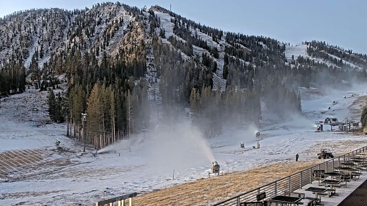 Snowmaking machines operating on ski slopes with mountains in background.