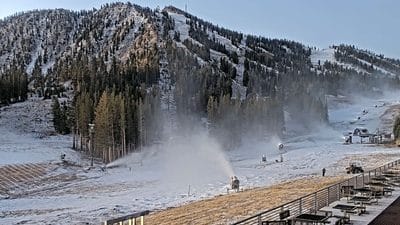Snowmaking machines operating on ski slopes with mountains in background.