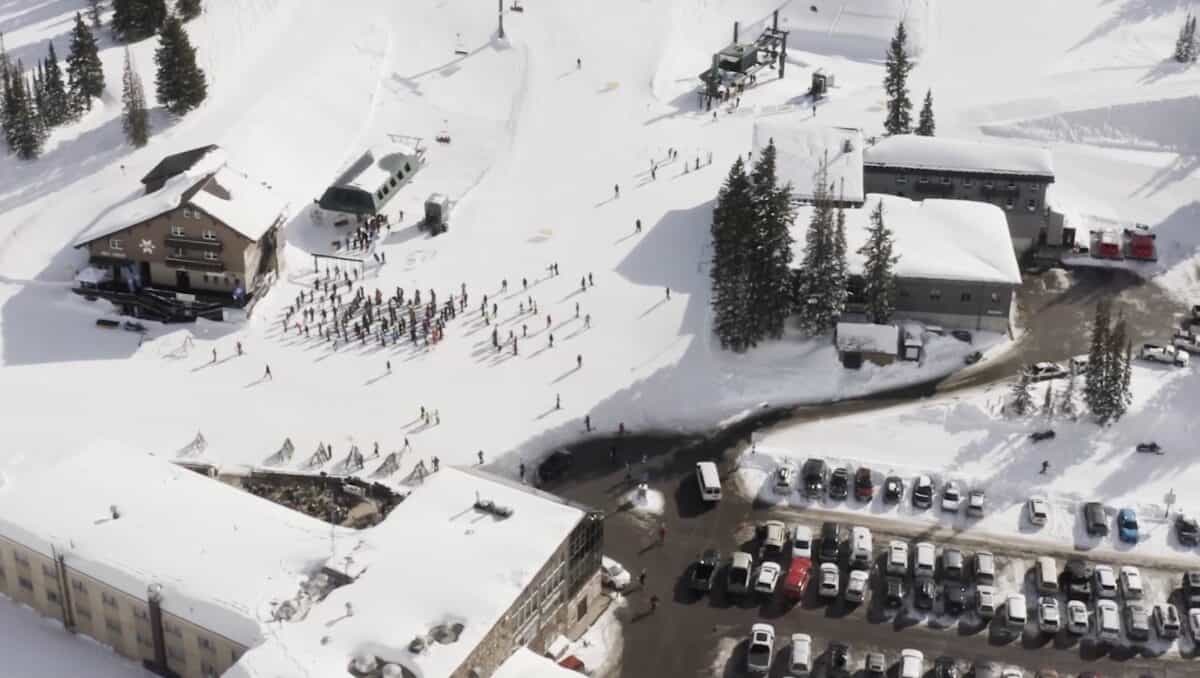 Aerial view of a snow-covered mountain resort with parking lot and ski lifts.