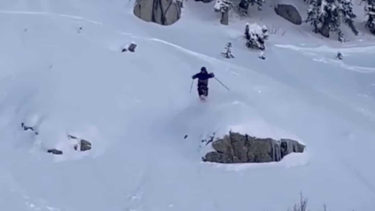Skier skiing through deep snow on a mountain with rocks and trees around.