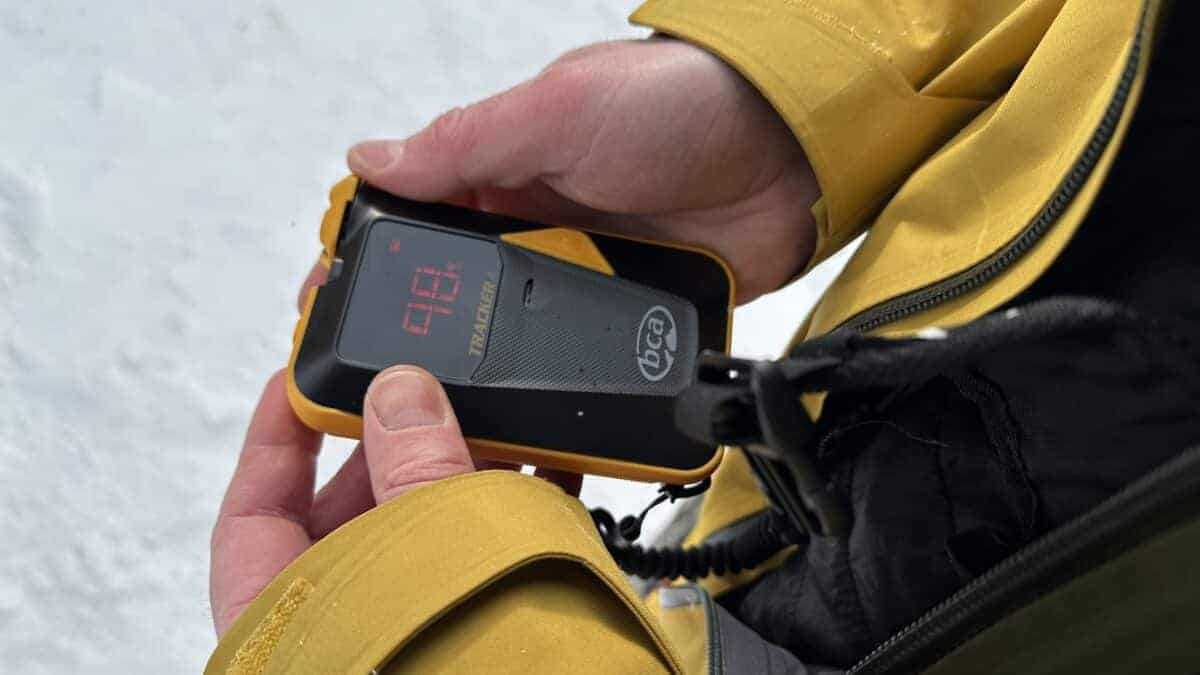 Person using a portable breathalyzer device outdoors in mountain terrain.