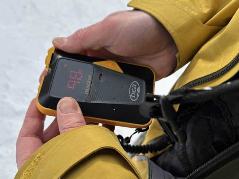 Person using a portable breathalyzer device outdoors in mountain terrain.