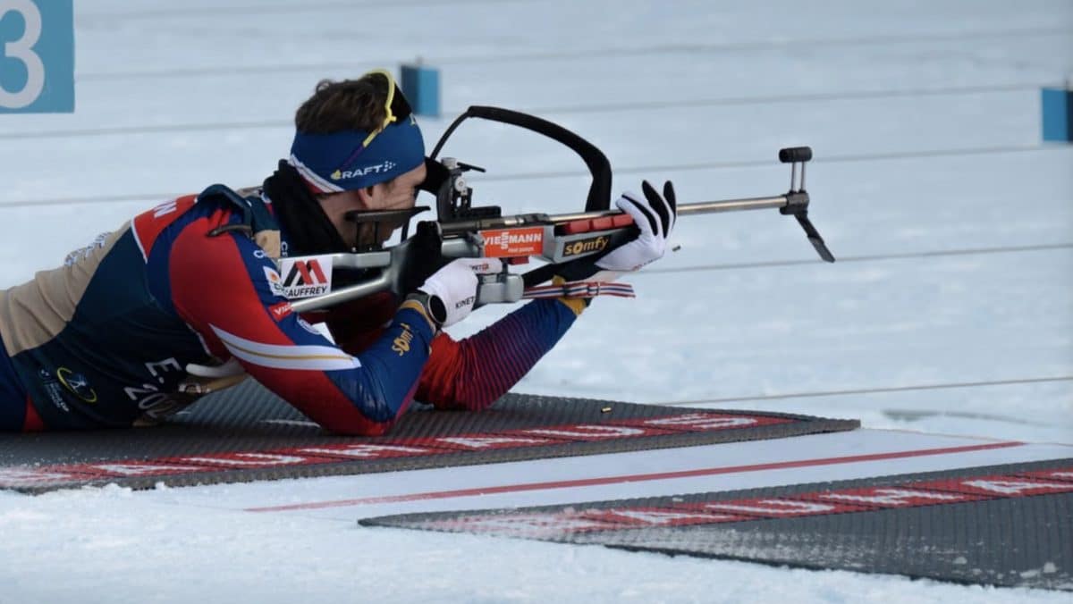Biathlon athlete aiming rifle during winter race on snow.