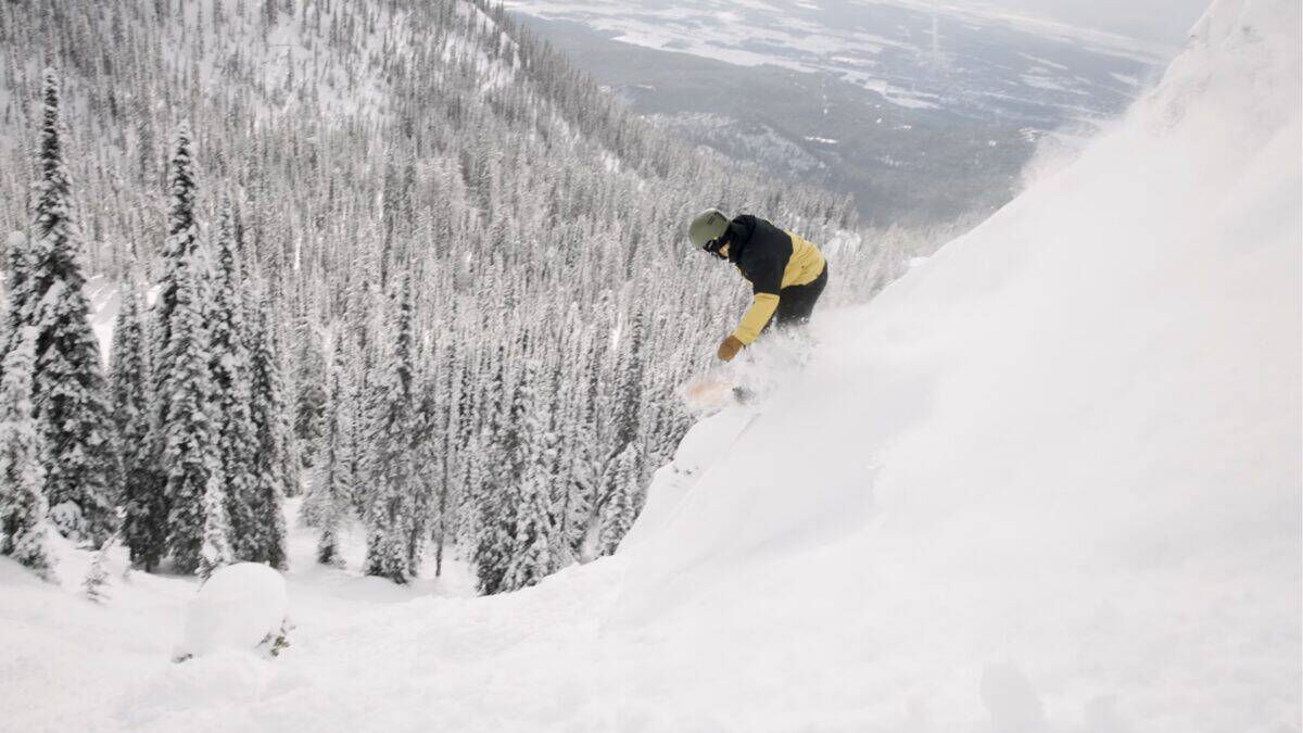Snowboarder carving through fresh powder on a mountain slope.