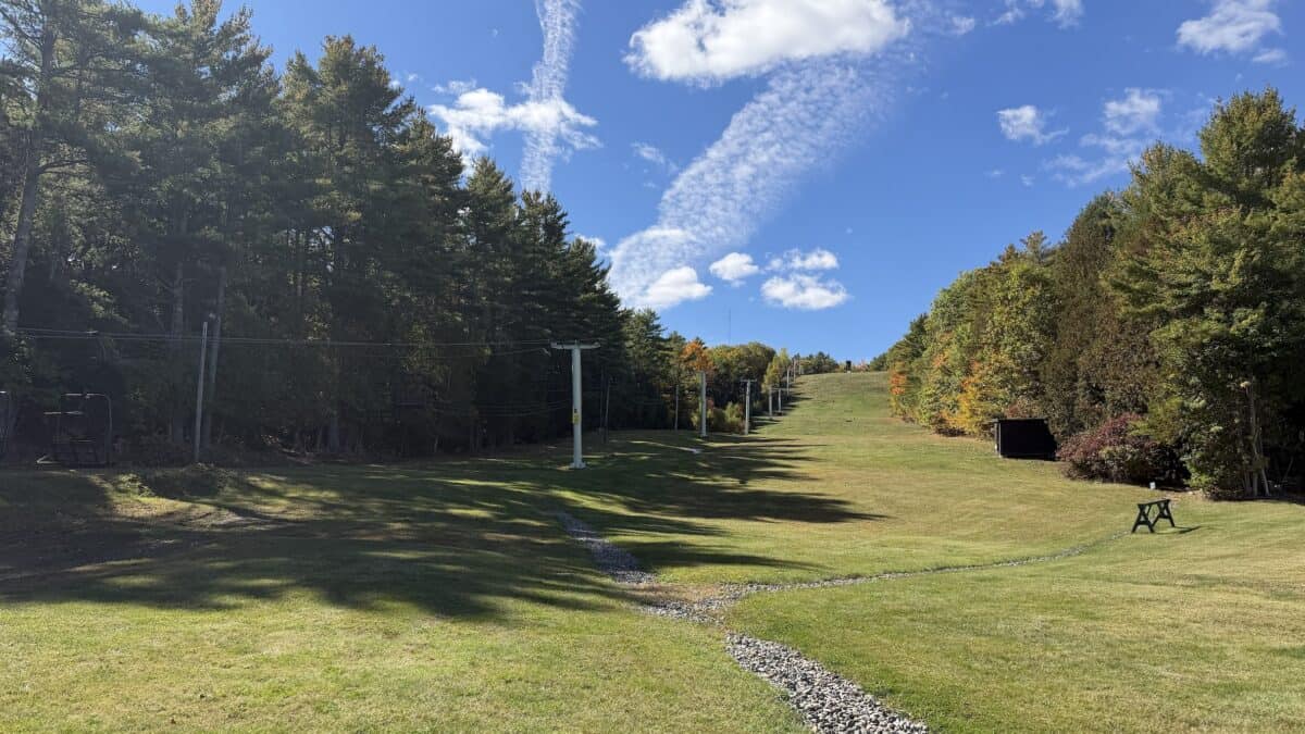 Empty ski lift area in Maine with green trees and blue sky.