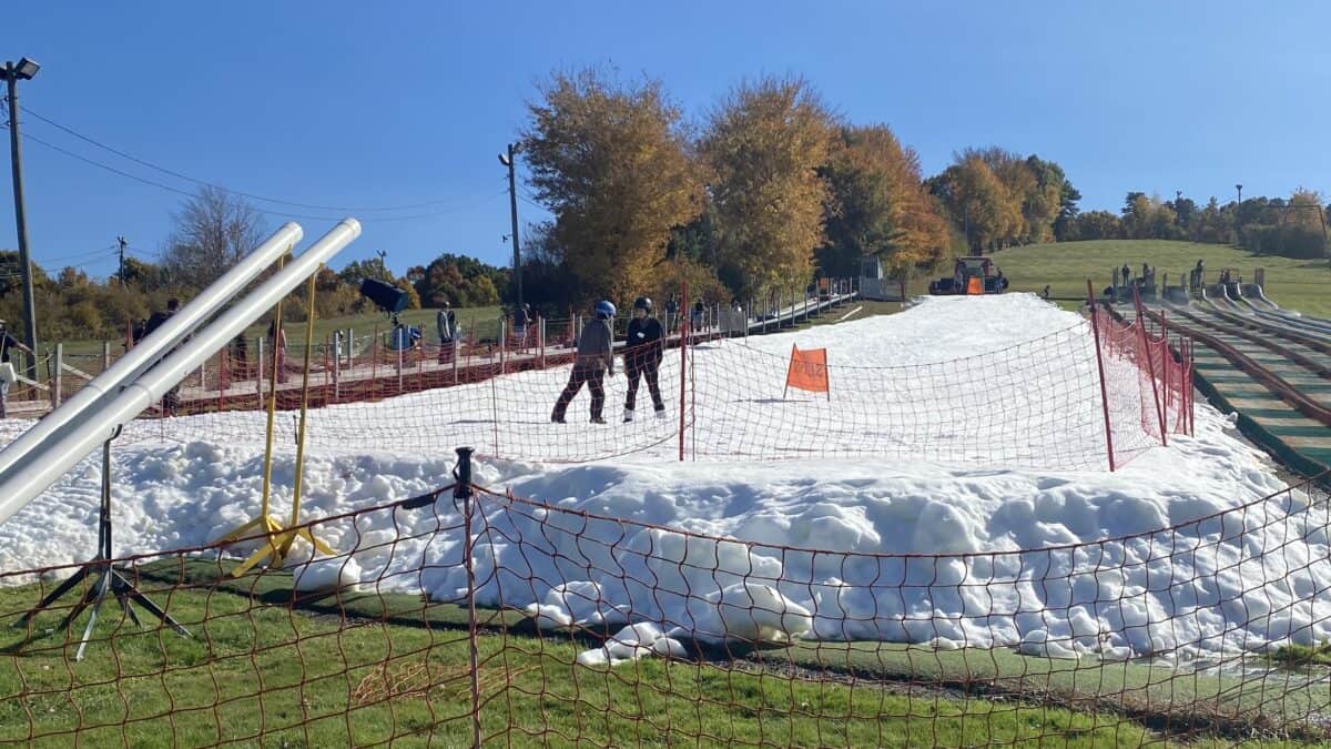 Snow-covered slope under clear blue sky with skiers and orange safety netting.