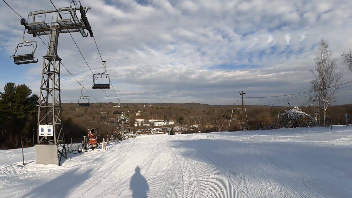 Snowy mountain ski slope with chairlift and distant trees.