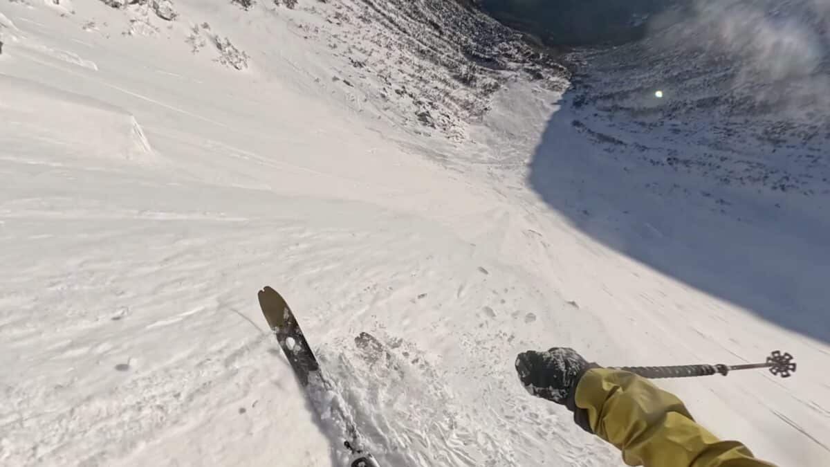 Skier descending a steep snowy slope with a ski pole in view.