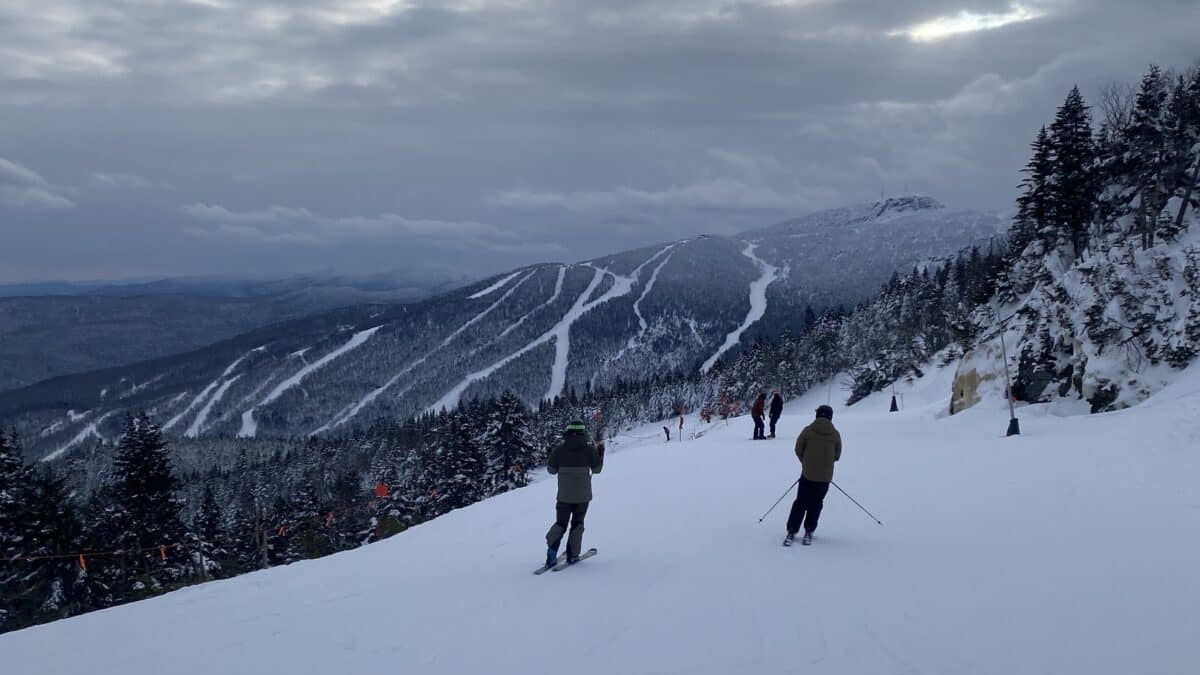 Skier on a snowy mountain slope with trees and chairlift in distance.