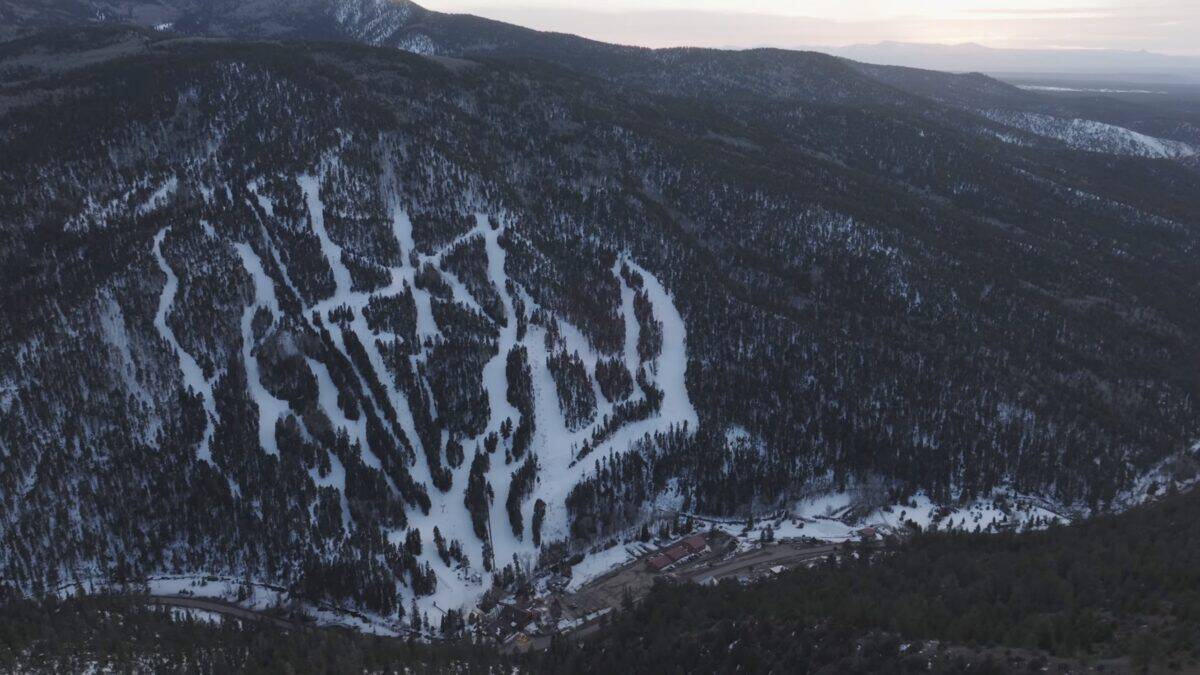 Snow-covered ski trails winding through a forested mountain landscape.