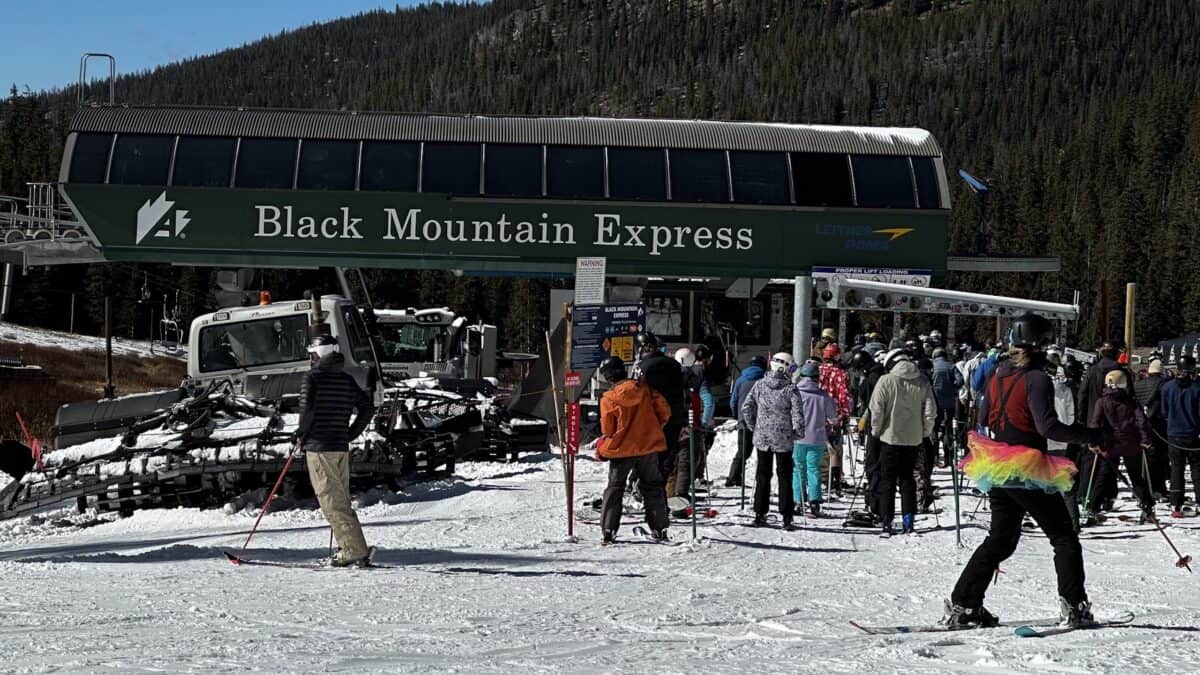 Skiers and boarding crowd at Black Mountain Express base in snowy mountain town.