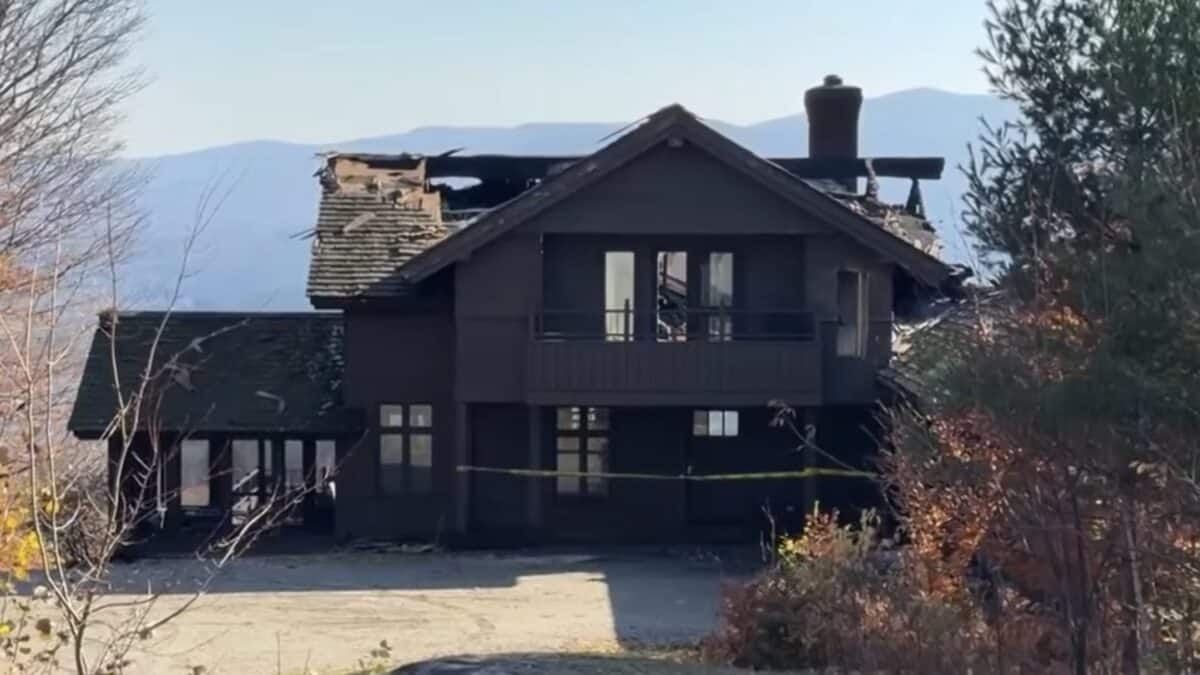 Charred mountain cabin with partially collapsed roof and smoke damage.