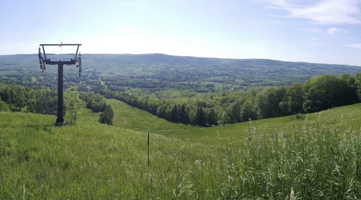 Scenic hillside with chairlift in a green valley under a blue sky.