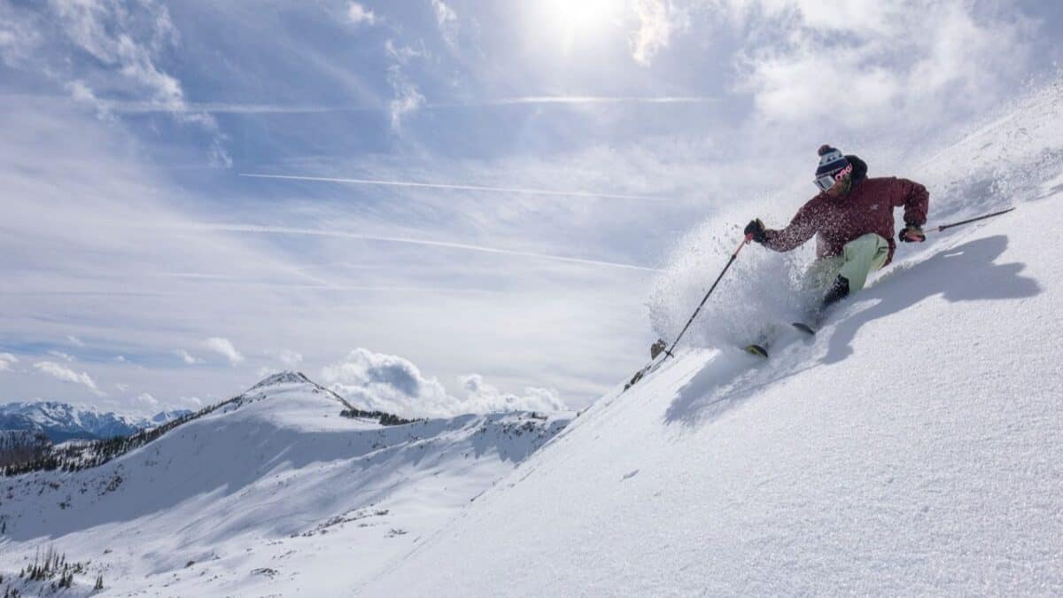 Skier descending a snowy mountain slope with a clear blue sky.