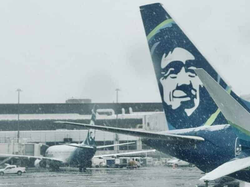 Alaska Airlines aircraft parked at the airport during snowy weather.